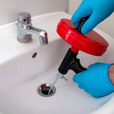 Plumbing issues, occupation in sanitation and handyman contractor concept with plumber repairing drain with plumbers snake (steel spiral that twists through pipes to collect dirt) in residential sink